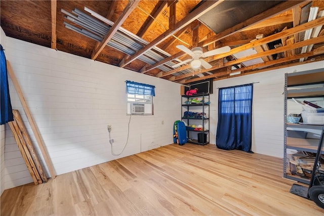 basement with light wood-type flooring, cooling unit, wooden walls, and ceiling fan