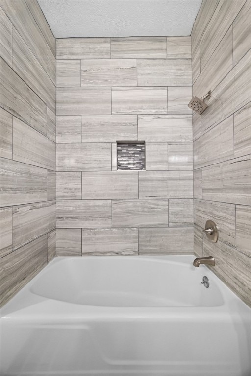 bathroom with a textured ceiling and tiled shower / bath