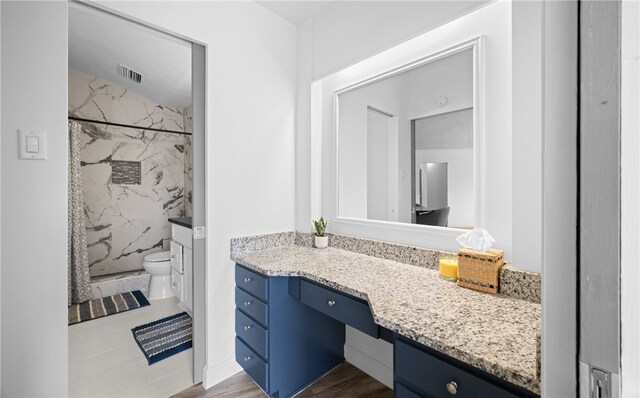 bathroom featuring vanity, toilet, wood-type flooring, and tiled shower