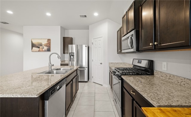 kitchen with a center island with sink, light stone counters, sink, light tile patterned floors, and appliances with stainless steel finishes