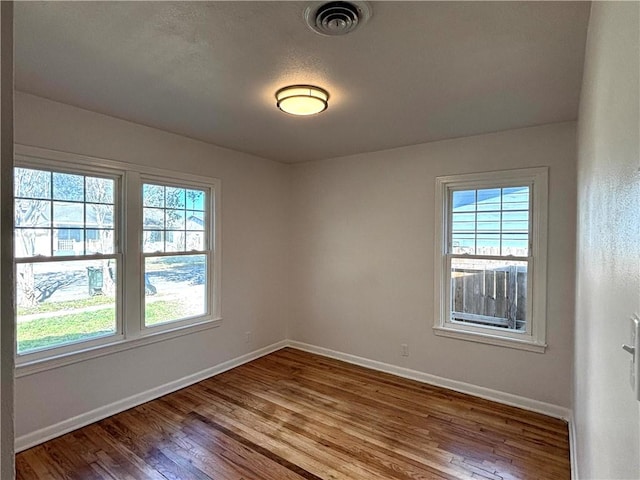 unfurnished room featuring baseboards, visible vents, a wealth of natural light, and wood finished floors