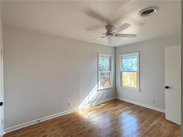 empty room with visible vents, ceiling fan, baseboards, and wood finished floors