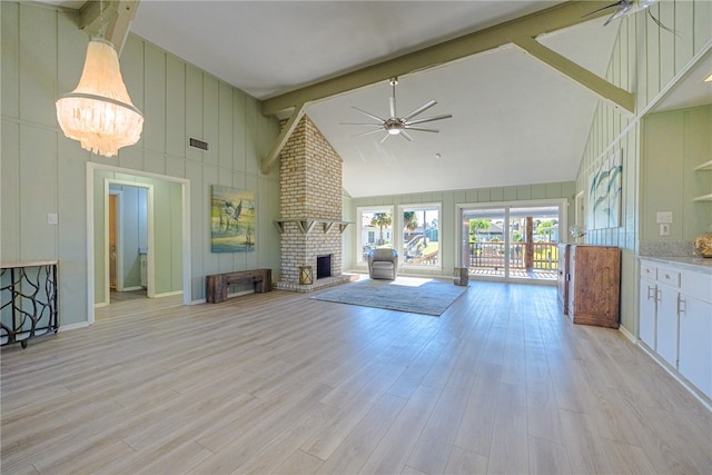 unfurnished living room with a brick fireplace, beam ceiling, high vaulted ceiling, an inviting chandelier, and light hardwood / wood-style floors