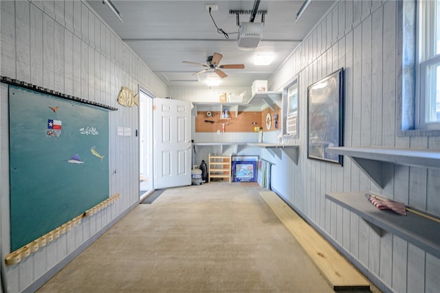 interior space featuring a garage door opener, ceiling fan, and wood walls