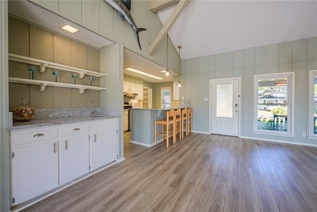 kitchen with decorative light fixtures, light hardwood / wood-style floors, a kitchen breakfast bar, and white cabinetry