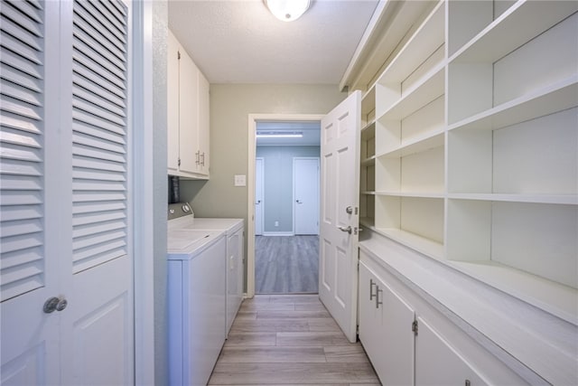 washroom featuring washer and clothes dryer, cabinets, light wood-type flooring, and a textured ceiling