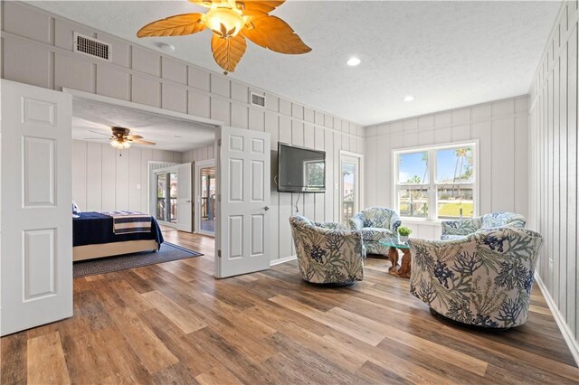 bedroom with ceiling fan, wood walls, wood-type flooring, a textured ceiling, and access to outside