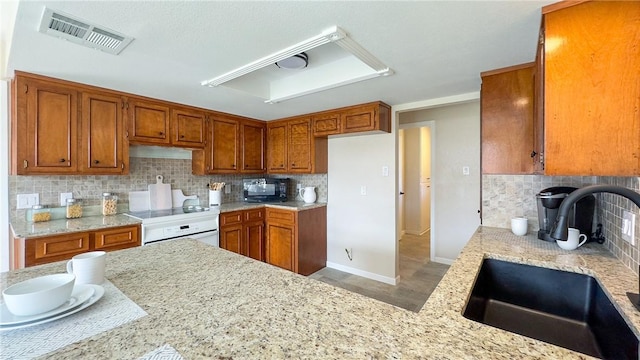 kitchen with light stone counters, sink, decorative backsplash, and oven