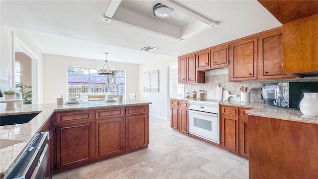 kitchen with decorative light fixtures, tasteful backsplash, sink, oven, and a raised ceiling