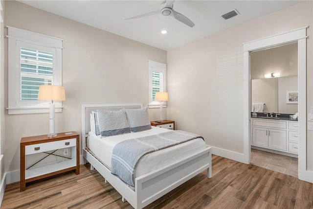 bedroom with multiple windows, wood-type flooring, connected bathroom, and ceiling fan