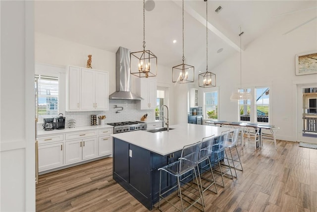 kitchen featuring sink, wall chimney range hood, white cabinets, range, and an island with sink