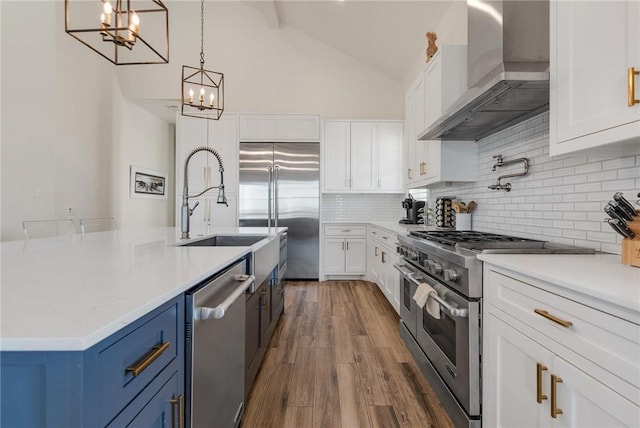 kitchen with blue cabinetry, white cabinetry, wall chimney exhaust hood, premium appliances, and decorative light fixtures