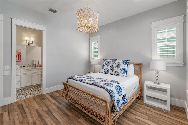 bedroom with a chandelier, ensuite bathroom, multiple windows, and hardwood / wood-style flooring