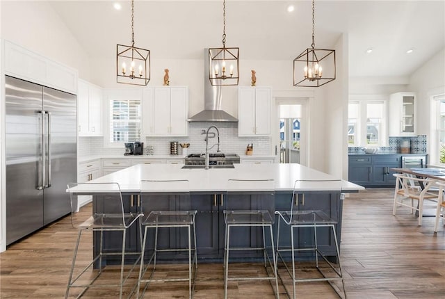 kitchen with a breakfast bar area, built in refrigerator, white cabinetry, hanging light fixtures, and a large island