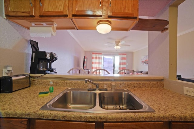 15426 Fortuna Bay Dr Unit 103, Corpus Christi, TX 78418 - kitchen with a sink, crown molding, ceiling fan, brown cabinetry, and a textured wall