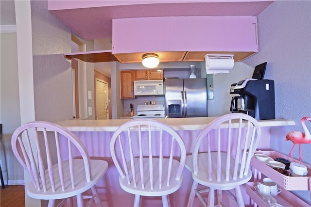 kitchen with a kitchen breakfast bar, white appliances, kitchen peninsula, and hardwood / wood-style flooring