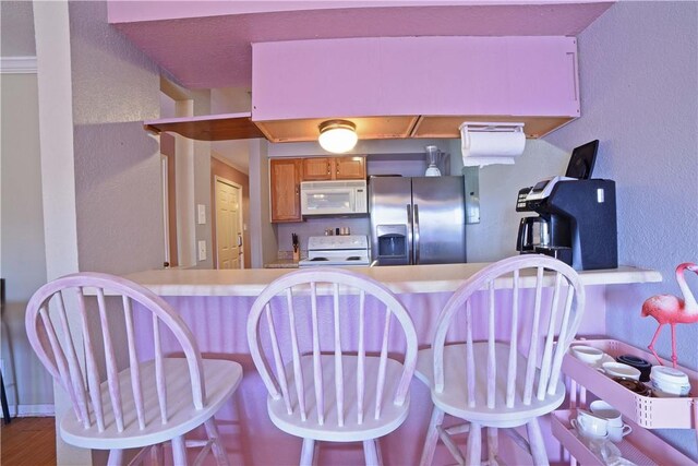 15426 Fortuna Bay Dr Unit 103, Corpus Christi, TX 78418 - kitchen featuring white appliances, a textured wall, brown cabinets, a peninsula, and a kitchen breakfast bar