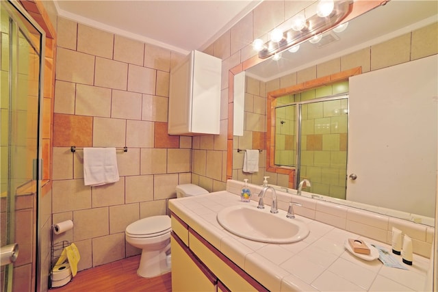 bathroom featuring hardwood / wood-style flooring, ornamental molding, a shower with shower door, toilet, and tile walls