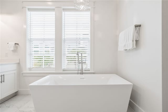 full bathroom featuring marble finish floor, baseboards, a freestanding bath, and vanity