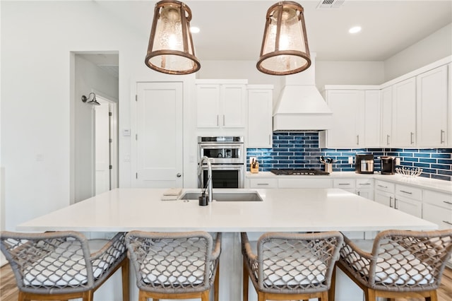 kitchen featuring pendant lighting, light countertops, stainless steel double oven, an island with sink, and a kitchen bar