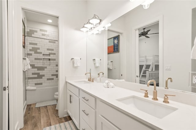 bathroom featuring a ceiling fan, double vanity, a sink, and wood finished floors