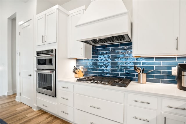 kitchen featuring light wood-style flooring, white cabinetry, light countertops, appliances with stainless steel finishes, and custom range hood