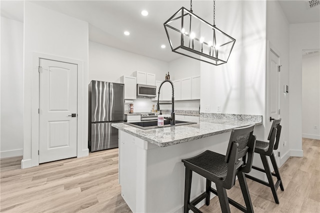 kitchen with kitchen peninsula, stainless steel appliances, decorative light fixtures, light hardwood / wood-style floors, and white cabinetry