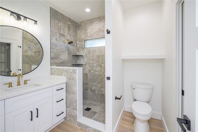 bathroom featuring wood-type flooring, vanity, toilet, and a tile shower