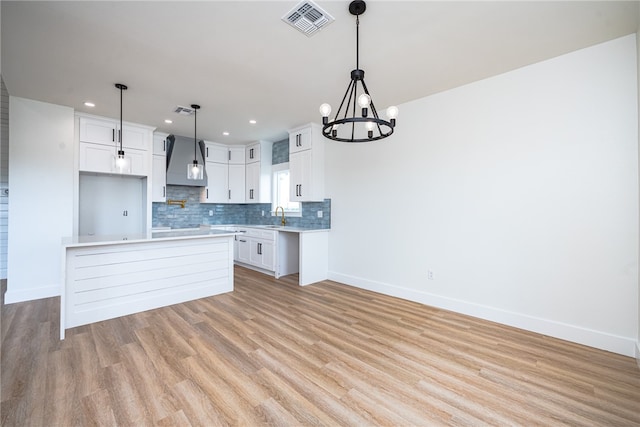 kitchen with light hardwood / wood-style floors, white cabinets, hanging light fixtures, sink, and a kitchen island