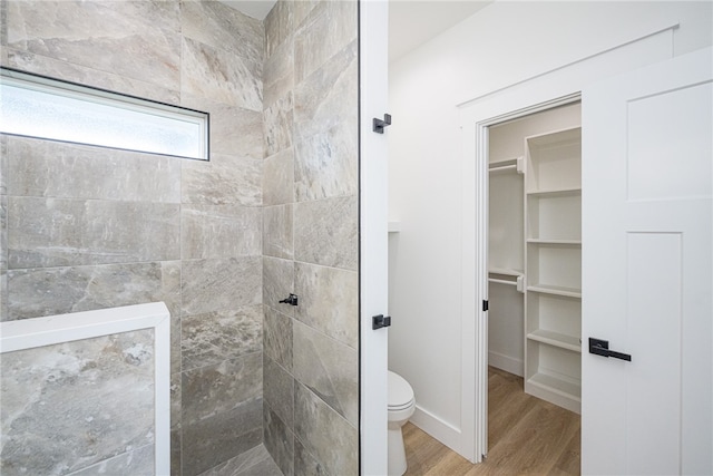 bathroom with toilet, hardwood / wood-style floors, and a tile shower