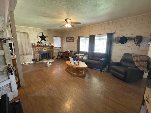 living room with a textured ceiling, wood-type flooring, ceiling fan, and a brick fireplace