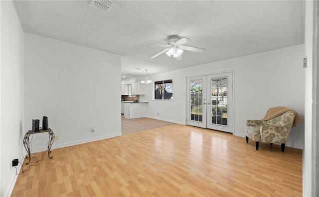 living room with ceiling fan with notable chandelier, light hardwood / wood-style floors, a textured ceiling, and french doors