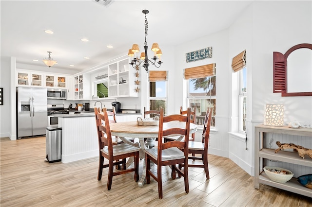 dining space with light wood-type flooring, sink, and a notable chandelier