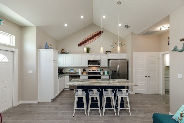 kitchen with a center island, high vaulted ceiling, a breakfast bar, white cabinetry, and appliances with stainless steel finishes