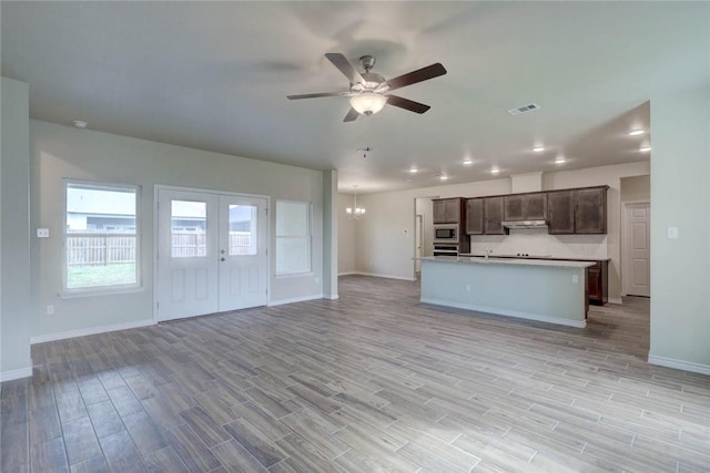 kitchen featuring french doors, an island with sink, ceiling fan with notable chandelier, dark brown cabinetry, and stainless steel microwave