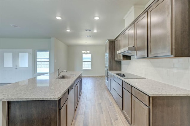 kitchen with light stone countertops, appliances with stainless steel finishes, light hardwood / wood-style floors, and an island with sink