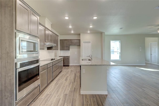 kitchen with appliances with stainless steel finishes, an island with sink, light stone countertops, ceiling fan, and sink