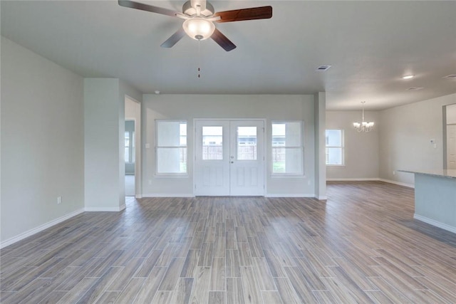 unfurnished living room with ceiling fan with notable chandelier, french doors, and light hardwood / wood-style flooring