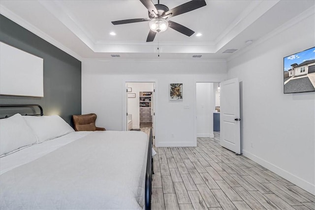 unfurnished bedroom with ceiling fan, crown molding, a tray ceiling, light wood-type flooring, and a walk in closet