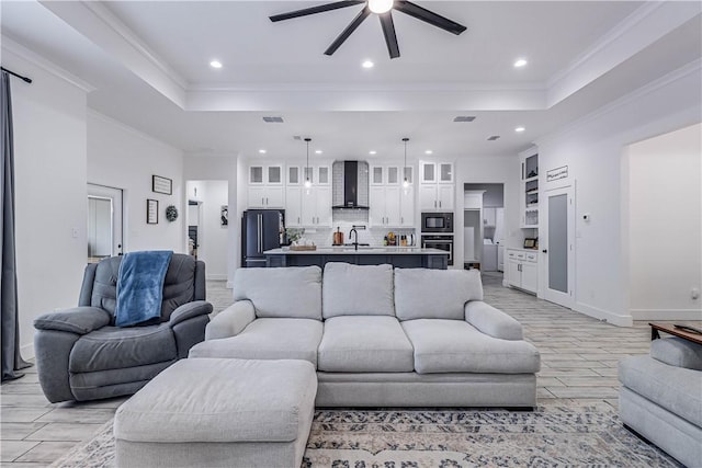 living room featuring ceiling fan, sink, a tray ceiling, and ornamental molding