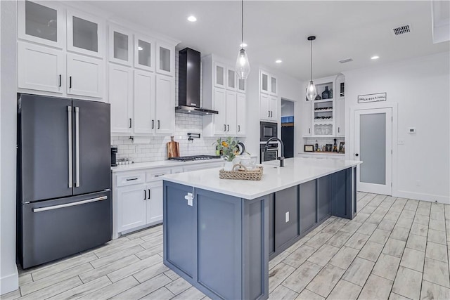 kitchen with white cabinets, appliances with stainless steel finishes, wall chimney exhaust hood, and a center island with sink