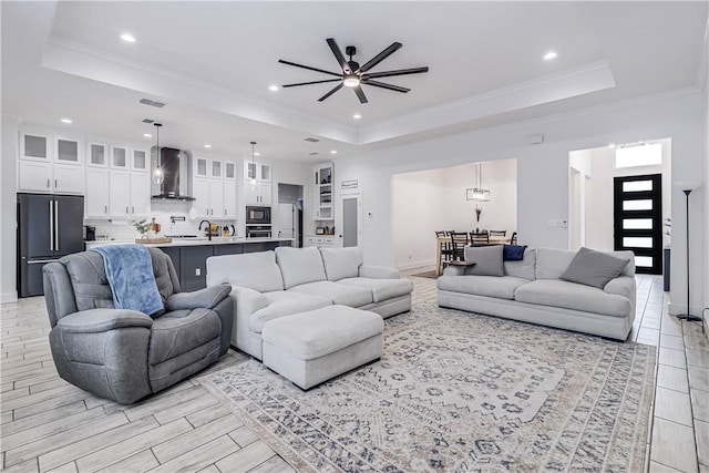 living room with a raised ceiling, ceiling fan, sink, and ornamental molding