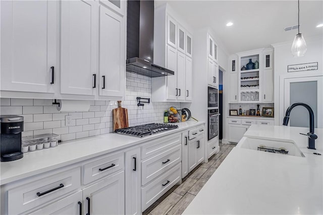 kitchen with stainless steel gas stovetop, white cabinetry, decorative light fixtures, wall chimney exhaust hood, and sink