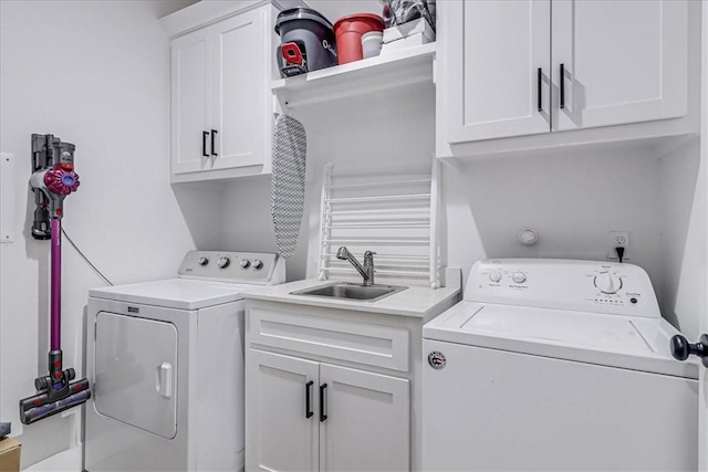 clothes washing area with washing machine and dryer, cabinets, and sink