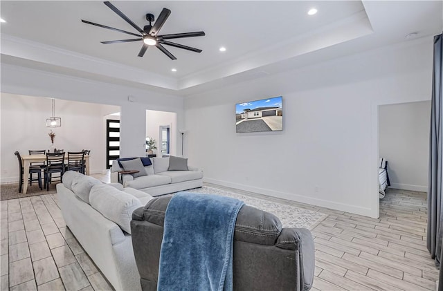 living room featuring ceiling fan, a tray ceiling, and ornamental molding