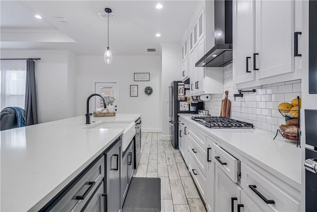 kitchen with decorative light fixtures, wall chimney range hood, white cabinets, and crown molding