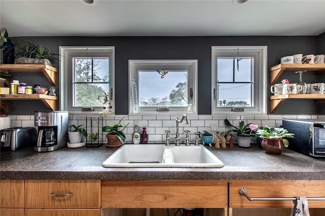 kitchen featuring brown cabinetry, dark countertops, a sink, and open shelves