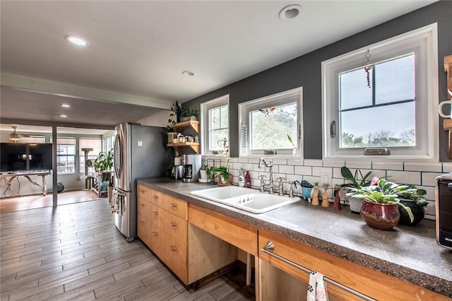 kitchen featuring decorative backsplash, dark countertops, freestanding refrigerator, light wood-type flooring, and a sink