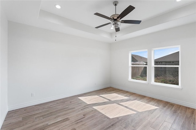 empty room featuring light hardwood / wood-style flooring, a raised ceiling, and ceiling fan