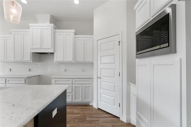 kitchen with dark wood-type flooring, built in microwave, decorative light fixtures, light stone counters, and white cabinetry